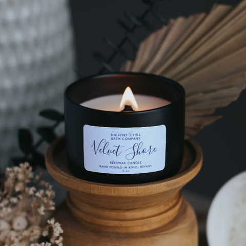 Black candle with a white label on a wooden holder, surrounded by decorative elements.