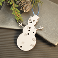 Metal snowman ornament with circuit board design on a textured surface with greenery.
