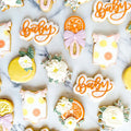 Decorative cookies with 'baby' text and floral designs on a marble surface