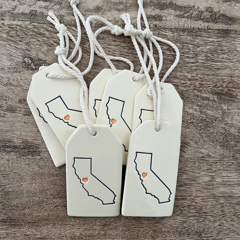 Four white tags with black outlines of California and orange hearts on a wooden surface