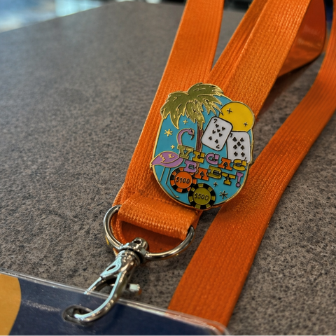 Orange lanyard with a colorful badge featuring palm trees and dice on a gray surface.