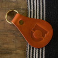 Brown leather keychain with a gold ring on a wooden surface