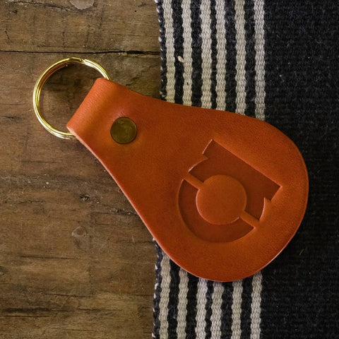 Brown leather keychain with a gold ring on a wooden surface