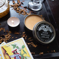 Sore Muscle Salve container with candles and tarot cards on a dark surface