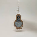 A small hanging ornament shaped like a pigeon, with a light blue-gray body, brown outline, and a white-and-brown string, shown against a plain light background. The text 'Standing Straight' appears in the lower right corner.