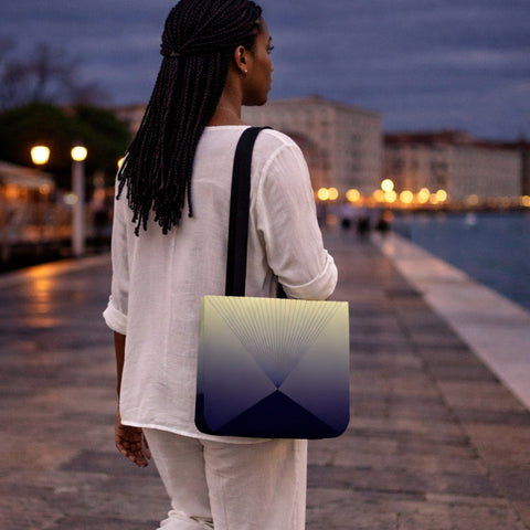Person walking along a waterfront promenade at dusk with a gradient bag.
