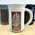 White mug with brown leaf design on a wooden surface