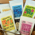 A set of Wild & Tea loose leaf herbal tea pouches arranged together, including Quiet Mind, Blue Chamomile, Tulsi Time, and Plum Rose Black Tea, alongside a small jar of honey and a metal tea infuser, set in a wooden box.