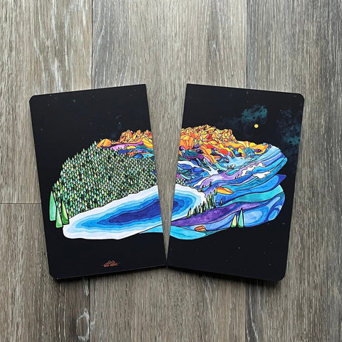 Two black cards with colorful mountain designs on a wooden surface