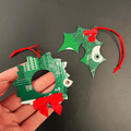 Hand holding a green circuit board Christmas ornament with red ribbons on a black background