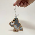 A hand holds a small ceramic bird ornament against a plain light background. The bird is light brown with gray wings and a pale blue belly, holding a small white cup.