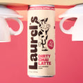 Can of Laurel's Dirty Chai Latte with a cow illustration on a pink background