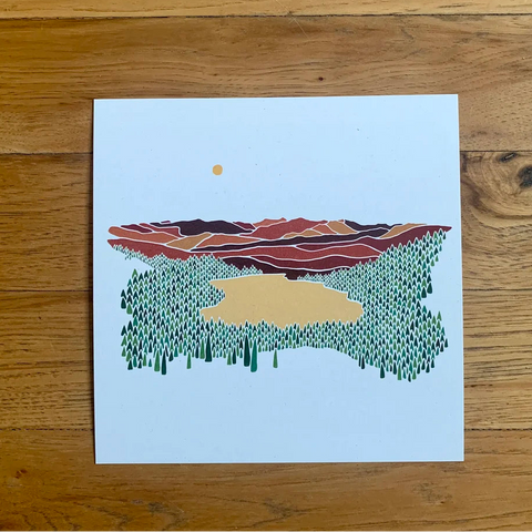 Art print of a stylized landscape with mountains and trees on a wooden surface