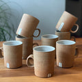 Set of brown mugs on a wooden table with a plant in the background