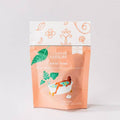 A stand-up pouch of Leaves of Leisure Bath Time tea, featuring a peach and white design with illustrations of tropical leaves and a woman relaxing in a bathtub.