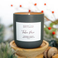 Candle labeled 'Tahoe Pine' from Hickory & Hill Bath Company on a wooden stand with a blurred background of greenery and berries.