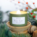 Green candle in a wooden holder with a blurred background of greenery and berries