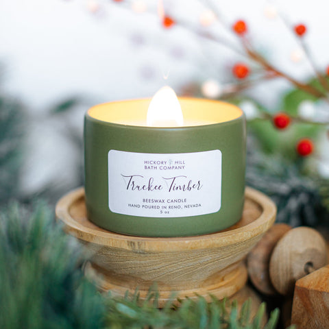 Green candle in a wooden holder with a blurred background of greenery and berries