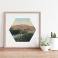 Hexagonal framed artwork of a landscape on a wall with decorative plants below.