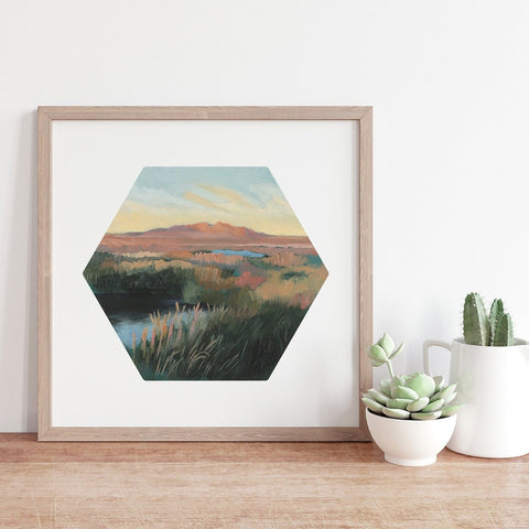 Hexagonal framed artwork of a landscape on a wall with decorative plants below.
