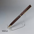 A walnut wood pen with gold-tone metal accents displayed on a clear acrylic stand against a neutral gray background. The word 'Walnut' is printed in black text in the bottom-left corner.