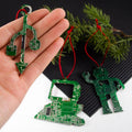 Hand holding a green circuit board ornament with more ornaments on a black surface.