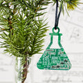Green electronic circuit board ornament shaped like a beaker hanging on a Christmas tree.