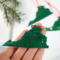 Hand holding a green electronic circuit board ornament with more ornaments in the background.