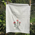 White towel with red floral design hanging on a clothesline outdoors