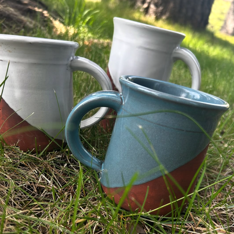 Three ceramic mugs with gradient designs on a grassy background