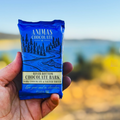 Hand holding a bar of Animas Chocolate Co. River Bottom Chocolate Bark with a scenic background.