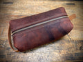 Brown leather pouch with a zipper on a wooden surface