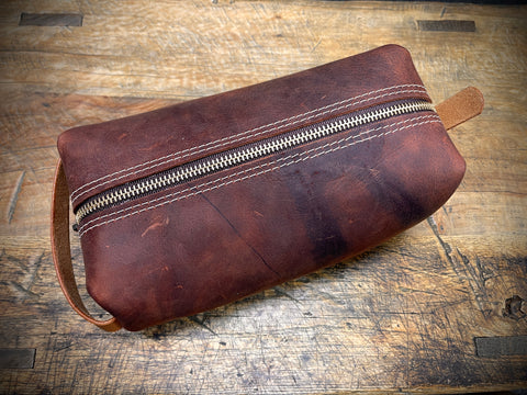 Brown leather pouch with a zipper on a wooden surface