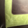 Green tote bag with brown leather patch and strap on a wooden surface