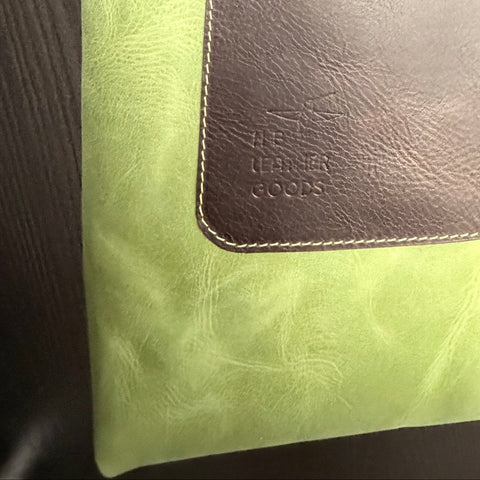 Green tote bag with brown leather patch and strap on a wooden surface