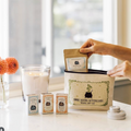 Three Sisters Apothecary travel gift set with a hand holding a package on a table.