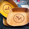 Two leather trays with engraved monograms on a workbench.