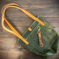Green tote bag with tan strap on a wooden surface