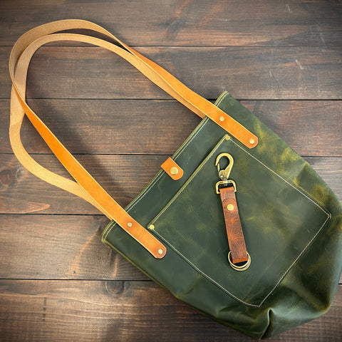Green tote bag with tan strap on a wooden surface