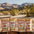 Four packages of 'Sweetpotato Awesome' snacks on a wooden surface with a mountainous background.