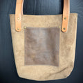 Beige tote bag with brown leather accents on a dark blue background