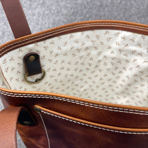 Close-up of a brown leather handbag with a textured interior on a gray surface.