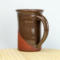 Brown ceramic mug with a handle on a wooden surface and light gray background