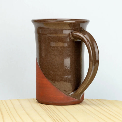 Brown ceramic mug with a handle on a wooden surface and light gray background