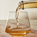 Glass being filled with a clear liquid from a bottle on a wooden surface.