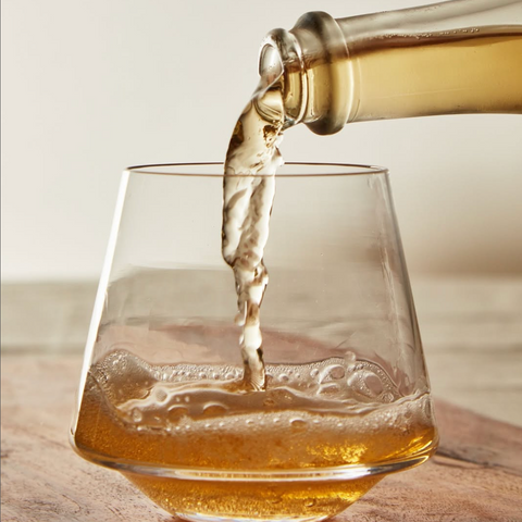 Glass being filled with a clear liquid from a bottle on a wooden surface.