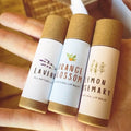 Three lip balm tubes labeled 'Lavender', 'Orange Blossom', and 'Lemon Rosemary' held in a hand.