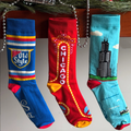 Three socks with different designs hanging on a string, featuring Old Style logo, Chicago sign, and Willis Tower.